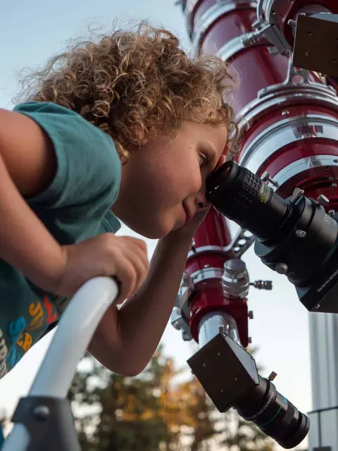 A child looks through a large telescope.