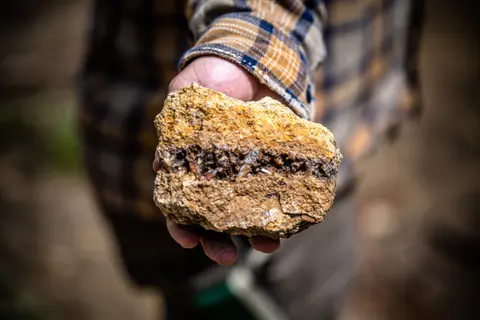 A person holds up a rock with crystals embedded in the middle.