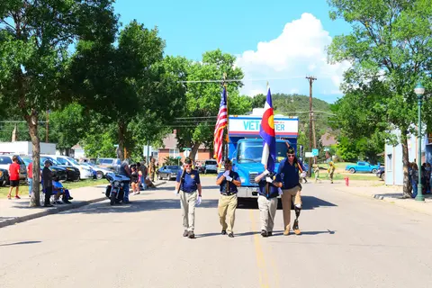 A color photograph of people walking in a parade holding flags down a street.