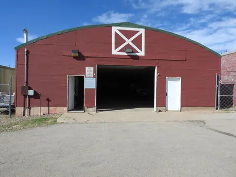 An exterior view of a red metal building with a large central opening and two white doors.