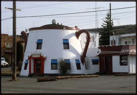 A unique building designed to look like a giant teapot stands near a road.
