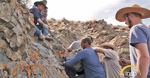 Several men work together to move a large rock on a hillside.