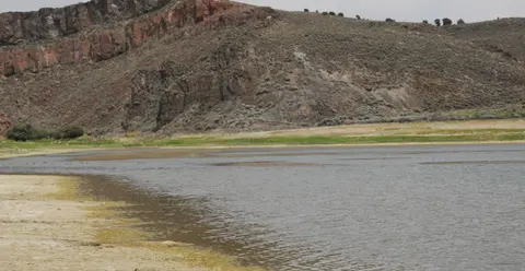 A river flows past a rocky hill and sandy shore.