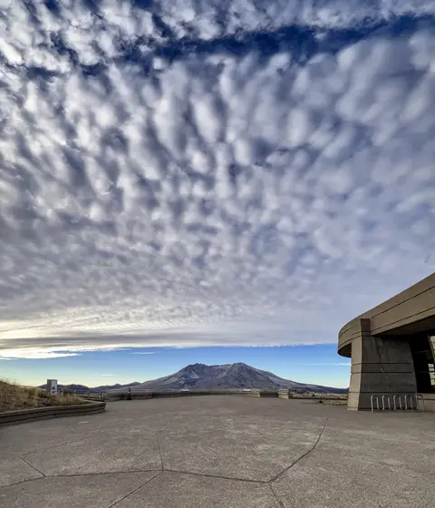 A wide-angle photo of a landscape with a large sky full of textured clouds and a building in the corner.