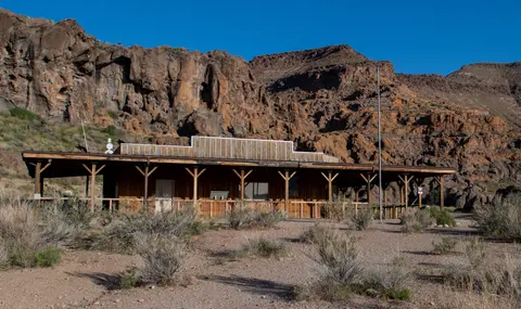 A wooden building sits in front of rocky cliffs.