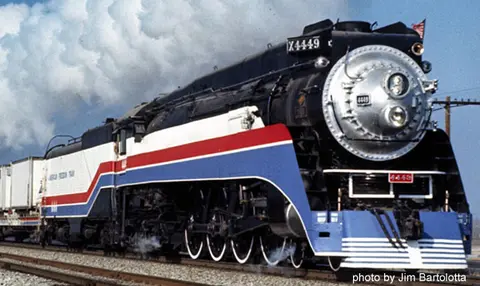 A large steam train painted in red, white, and blue colors is on the tracks.