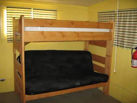 A wooden loft bed with a black futon underneath in a yellow room.