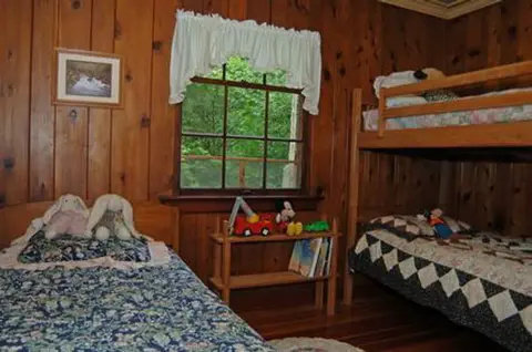 A rustic bedroom with wood-paneled walls, a single bed, and a set of bunk beds.