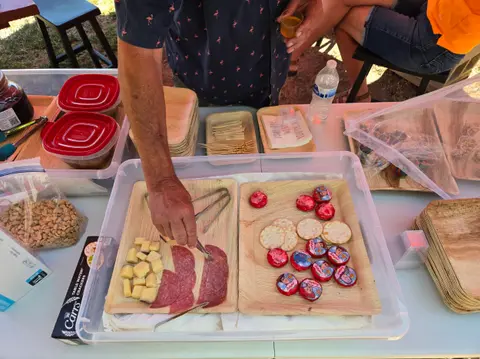 A person using tongs to pick up food from a snack spread.