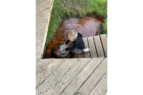 A child playing with water by a wooden boardwalk.