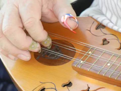 A close-up of a person playing a stringed instrument with fingerpicks.