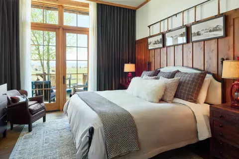 A rustic bedroom with a large bed, wooden paneling, and glass doors opening to an outdoor view.