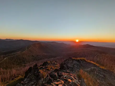 A sunset view over rolling mountains from a rocky peak.