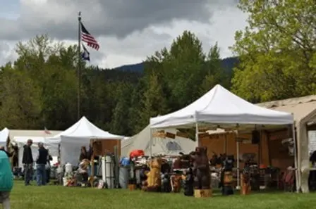 An outdoor market or fair with white tents set up on a grassy field.
