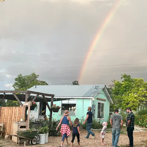 A group of people walk outside a light green building beneath a bright rainbow.