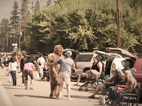 People gathered outdoors interacting with a person in a Sasquatch costume.