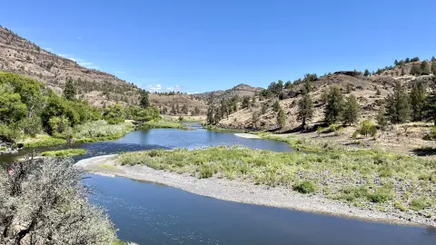 A wide river flowing through a dry, hilly landscape under a blue sky.