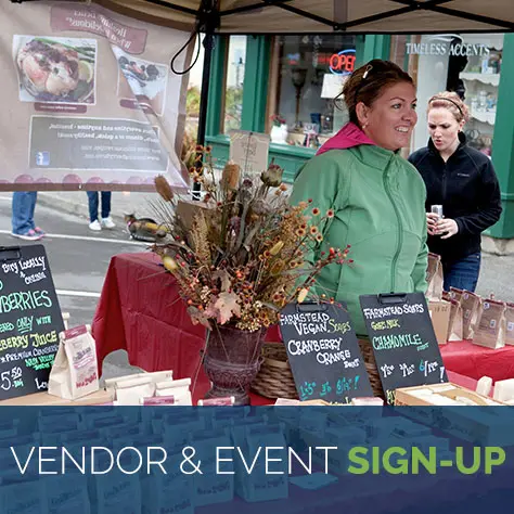 A vendor stands behind a market table displaying soaps and other goods.
