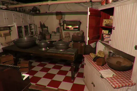 An old-fashioned kitchen interior with wooden cabinets, a table, and checkered flooring.
