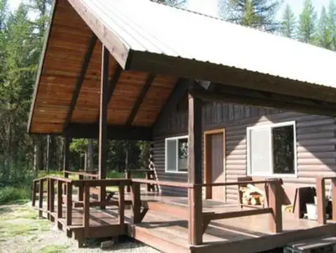 A wooden cabin with a large covered porch in a wooded area.