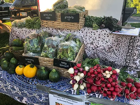 A farmers market table displays fresh vegetables and greens in baskets.