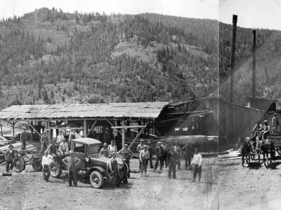Historic black and white photograph showing a lumber mill with workers and a truck.