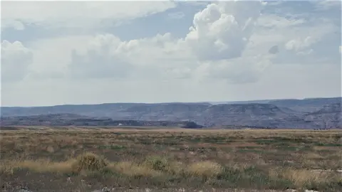 A wide landscape with a field in the foreground and distant hills under a cloudy sky.