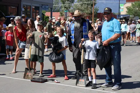 A group of people holding shovels and trash bags on a street during an outdoor event.