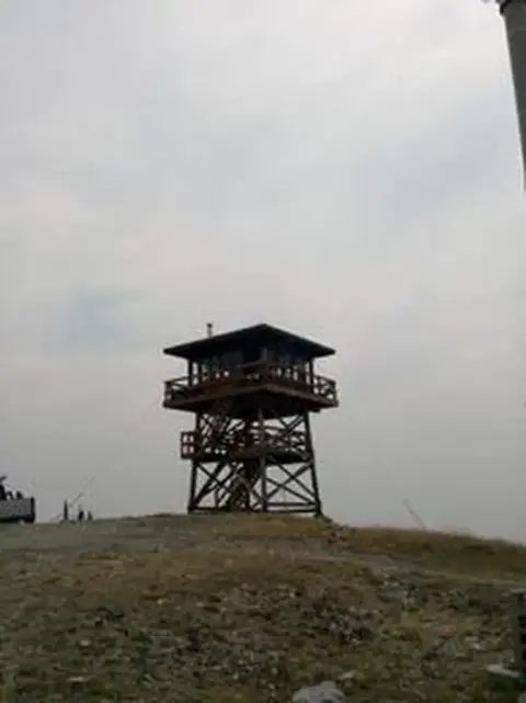 A wooden lookout tower stands on a hilltop under an overcast sky.