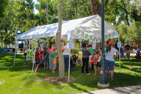 People gather under a white tent outdoors on a grassy area.