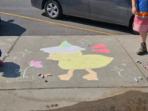A chalk drawing of a duck wearing a hat is on a concrete sidewalk.