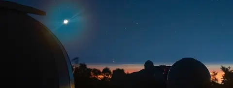 An astronomical observatory at night with domes against a starry sky and city lights on the horizon.