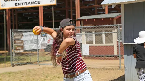 A young person throws a yellow ball outdoors.