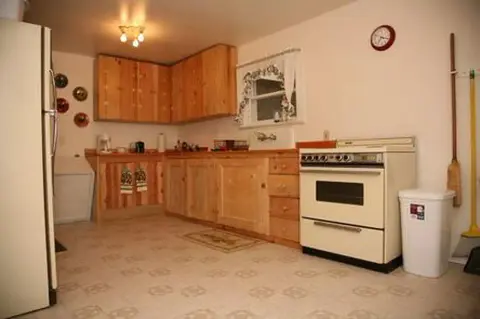 A simple kitchen features wooden cabinets, a white stove, and patterned linoleum flooring.