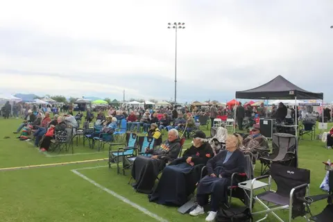 A crowd of people sitting in lawn chairs on a grassy field at an outdoor event.