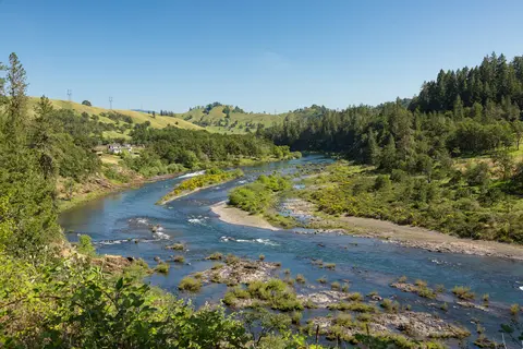 A winding river flows through a valley surrounded by green hills and trees.