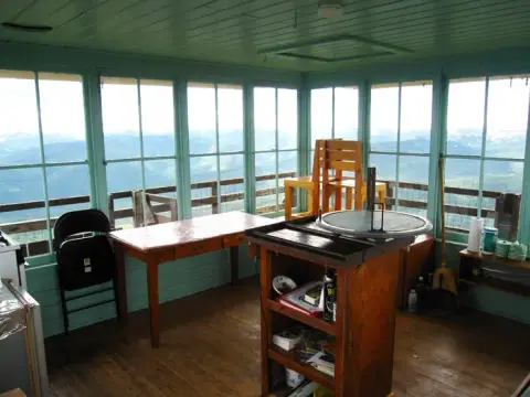 Interior of a small lookout tower with large windows looking out at mountains.