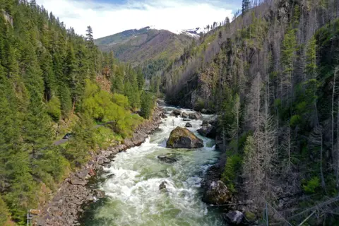 A fast-flowing river winds through a steep, forested mountain canyon.