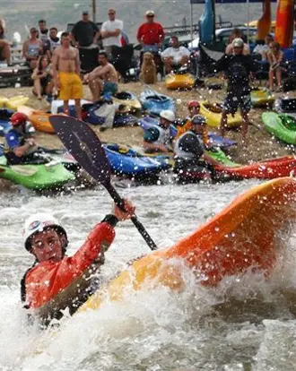 A kayaker navigates through rough water with spectators watching from the shore.