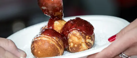 A person spoons jam onto a plate of round pastries.
