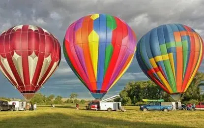 Three hot air balloons are prepared for flight in a grassy field.