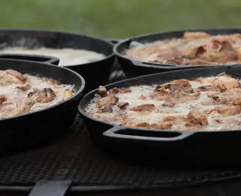 Cast iron pans filled with meat frying over an open fire.