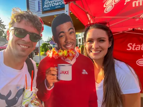 Two people pose next to a cutout figure holding a mug.