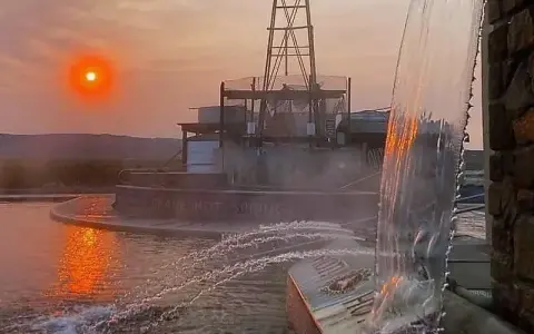 A hot spring pool with water cascading in the foreground during sunset.