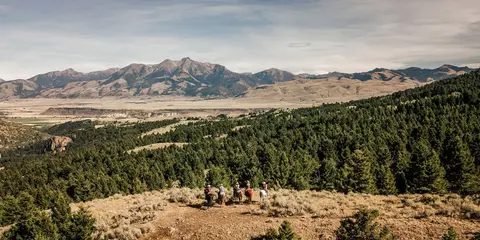 A group of horseback riders overlooking a vast valley and mountain range.