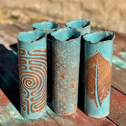 Five turquoise and brown ceramic vases stand on a wooden surface.