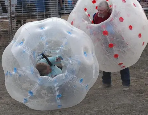 Two people participate in bubble ball sports outdoors.