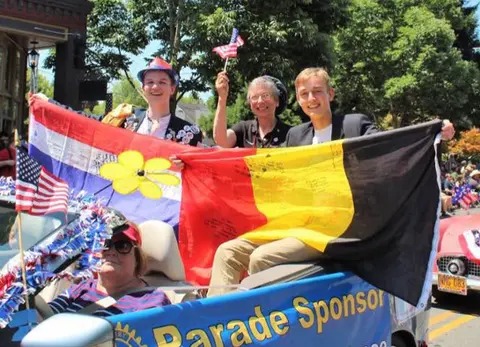 People ride in a convertible during a parade holding flags.