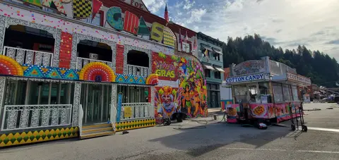 A colorful carnival funhouse and food booth stand outdoors.