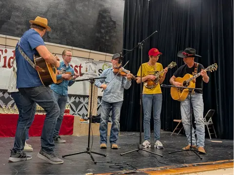 A band of musicians playing acoustic instruments on a stage indoors.